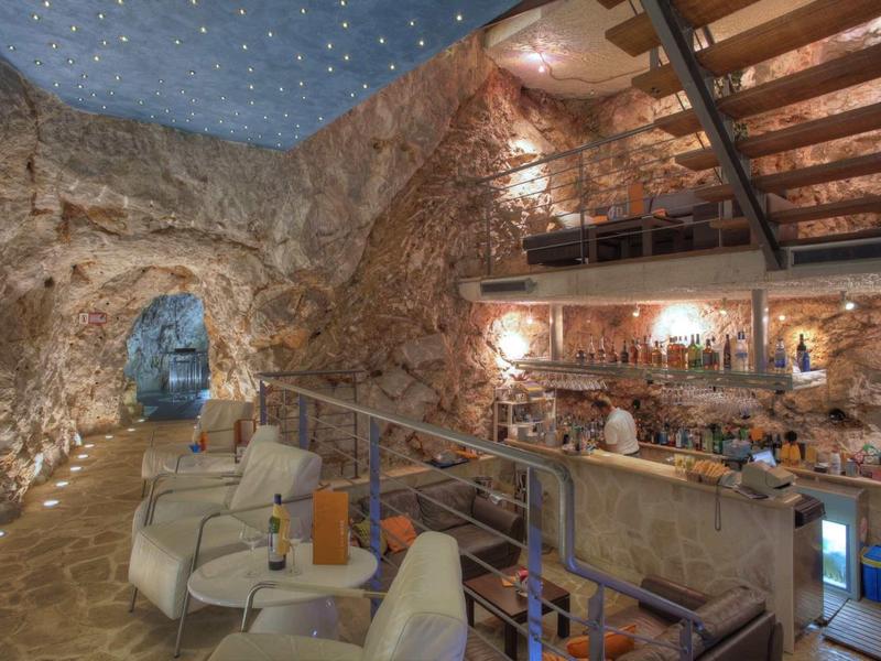 Unterirdische Bar in einem Höhlenraum mit felsigen Wänden, Stühlen und Treppe mit Beleuchtung.