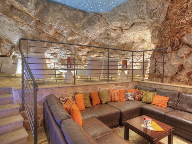 Gemütliche Sitzgruppe mit bunten Kissen in einer natürlichen Felsenhöhle mit moderner Beleuchtung.