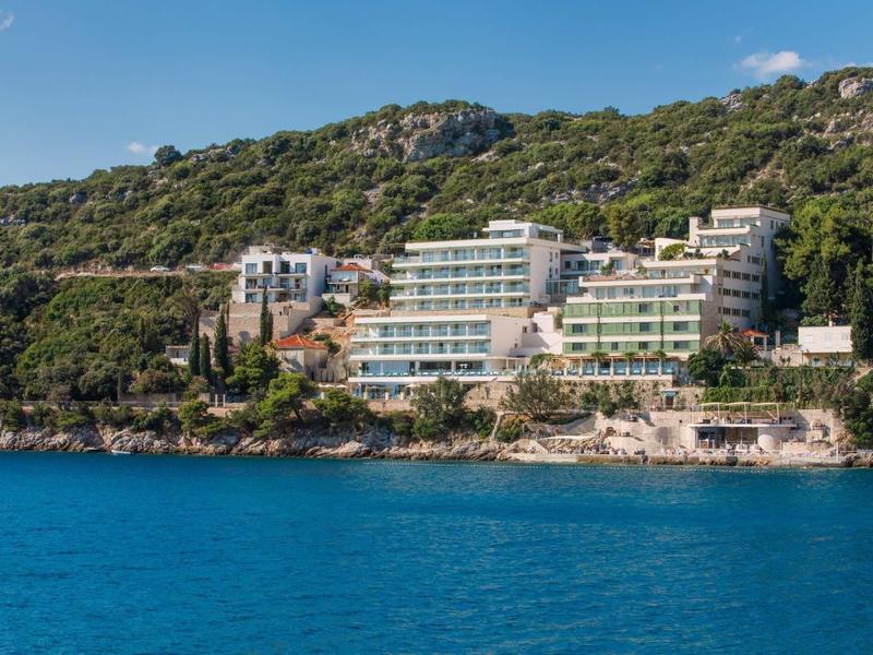 Mehrstöckiges Hotel am grünen Hügel mit Blick auf das blaue Meer und den klaren Himmel.