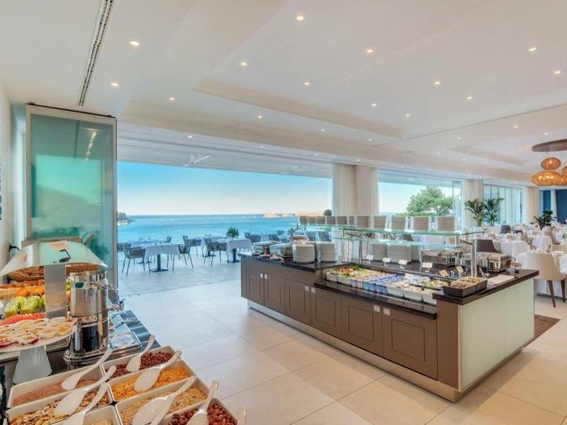 Modernes, helles Restaurant mit großen Fenstern, Meerblick, Buffet und gedeckten Tischen im Hintergrund.