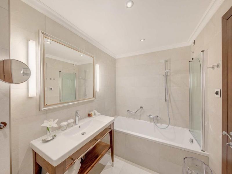 Helles Badezimmer mit weißer Badewanne, großem Spiegel und Doppelwaschbecken auf Holzgestell.