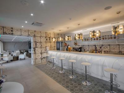 Nowoczesny bar hotelowy z długimi białymi ladami i białymi stołkami pod ciepłym oświetleniem.