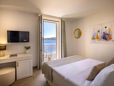 Bright hotel room with double bed, desk, TV, and balcony overlooking the sea.