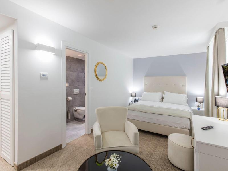 Modern hotel room with double bed, seating area, and open bathroom with shower.