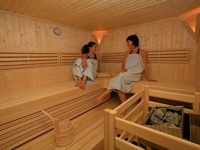 Twee vrouwen zitten en praten in een lichte houten sauna op houten banken.