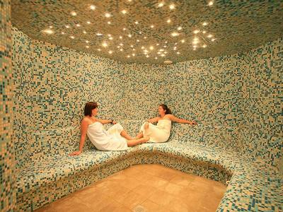 Twee vrouwen ontspannen in een stoomsaunaruimte met mozaïektegels en een sterrenhemel.