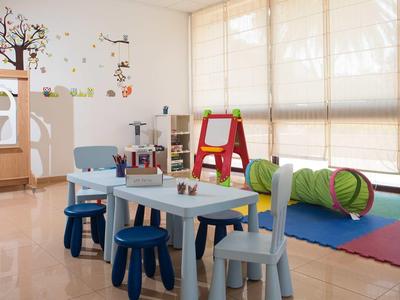 Lichte speelkamer voor kinderen met kleurrijke vloerkleden, tafels, stoelen en speelgoed.