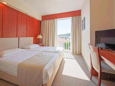 Lichte hotelkamer met tweepersoonsbed, bureau, tv en balkon met uitzicht.