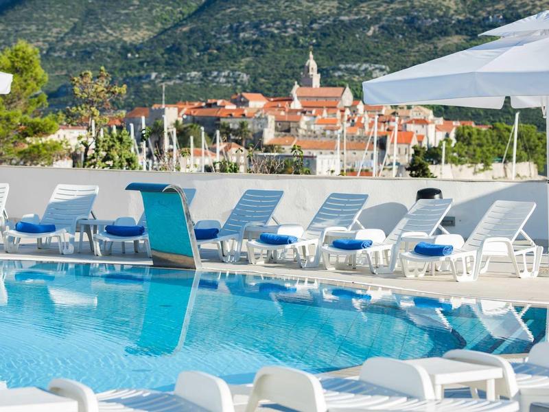 Zwembadgebied met ligstoelen en parasols tegen een berglandschap en stad.