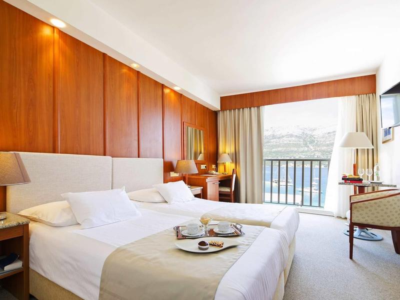 Lichte hotelkamer met twee eenpersoonsbedden, houten wanden en balkon met zeezicht.