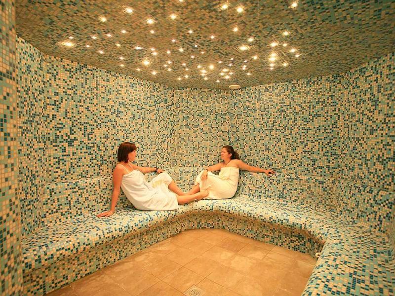 Twee vrouwen ontspannen in een stoomsaunaruimte met mozaïektegels en een sterrenhemel.