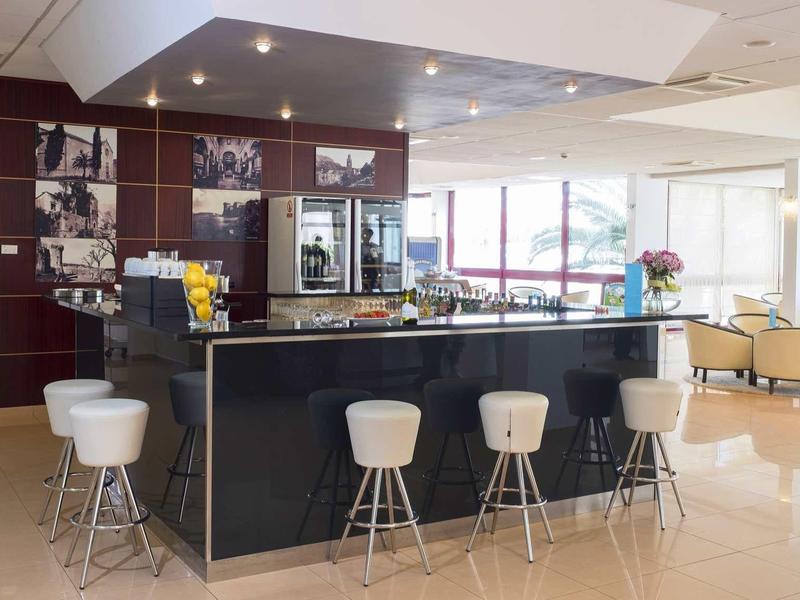 Moderne hotellounge met zwarte bar, witte barkrukken en comfortabele zithoeken.