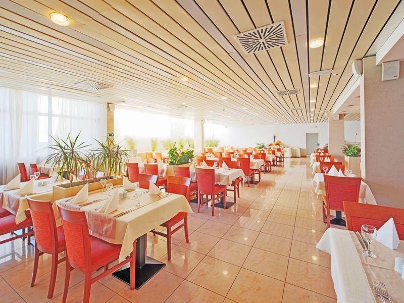 Licht hotelrestaurant met grote ramen, rode stoelen en gedekte tafels.