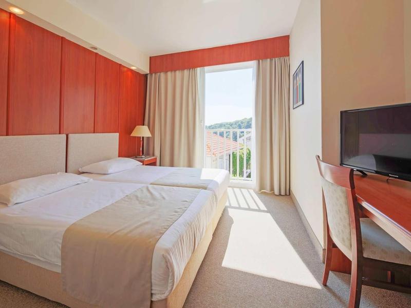 Lichte hotelkamer met tweepersoonsbed, bureau, tv en balkon met uitzicht.