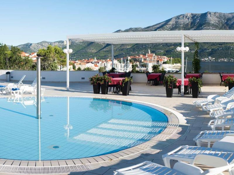Ronde buitenzwembad met ligstoelen en overdekte lounge, berglandschap op de achtergrond.