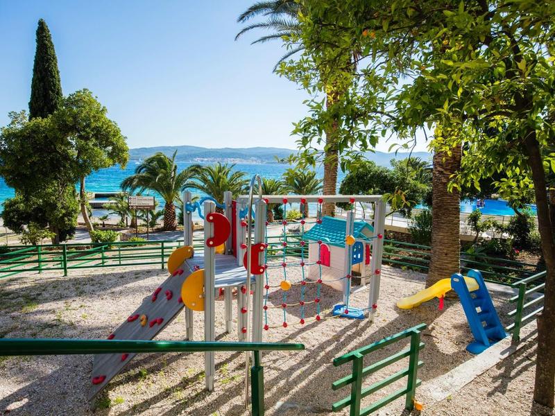 Speelplaats voor kinderen met glijbanen en klimrekken nabij de zee en palmbomen aan de kust.
