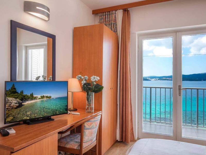 Hotelkamer met bureau, tv en balkon met uitzicht op zee.