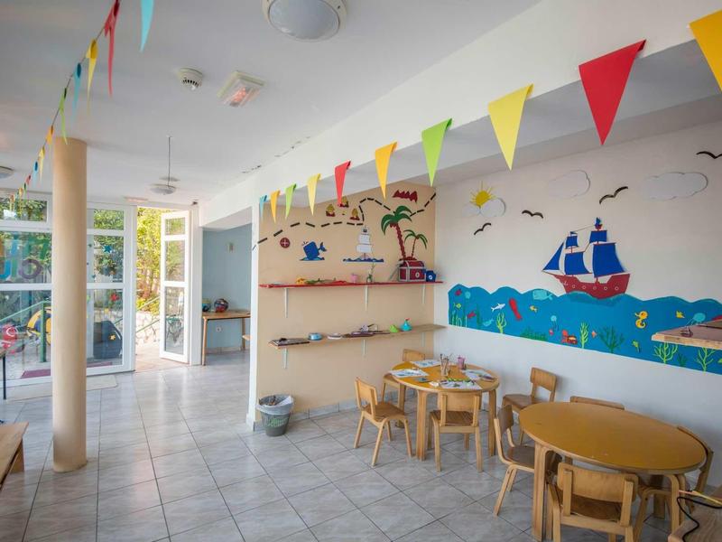 Kinderhoek met tafels, stoelen, kleurrijke vlaggen en muurschildering in lichte ruimte.