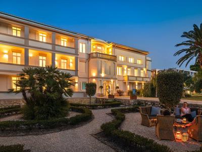 Edificio dell'hotel illuminato al crepuscolo con giardino e palme in primo piano.