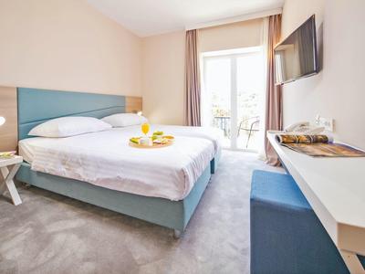 Helles Hotelzimmer mit Doppelbett, Fernseher, Schreibtisch und Balkon.