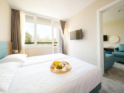 Helles Hotelzimmer mit Doppelbett und Frühstückstablett, Blick ins angrenzende Wohnzimmer.