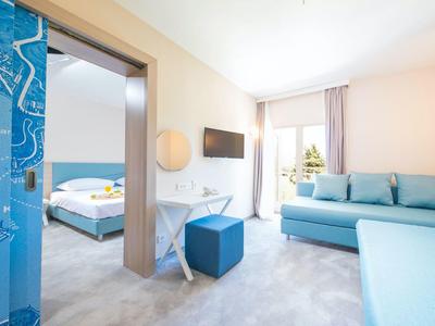 Helles Hotelzimmer mit blauen Möbeln, Sofa, Bett und Balkon mit Meerblick.