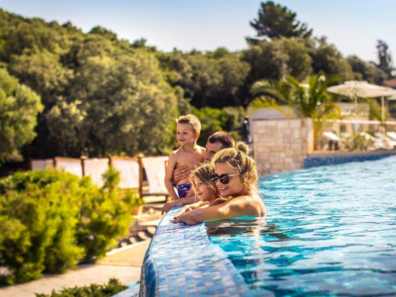Menschen, die am Rand eines Außenpools in sonnigem Hotelgarten entspannen.