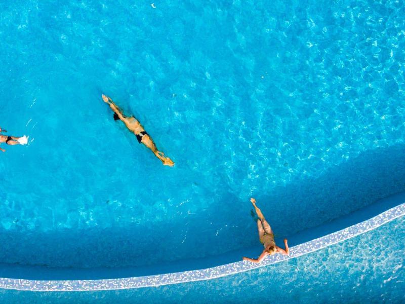 Drei Personen genießen das Schwimmen in einem großen blauen Pool mit klarem Wasser.