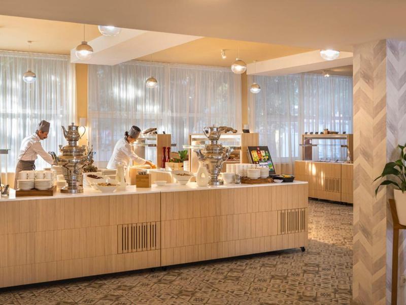 Helle Hotellobby mit Buffetbereich, Gästen und Personal, modernes Design mit Holz und Glas.