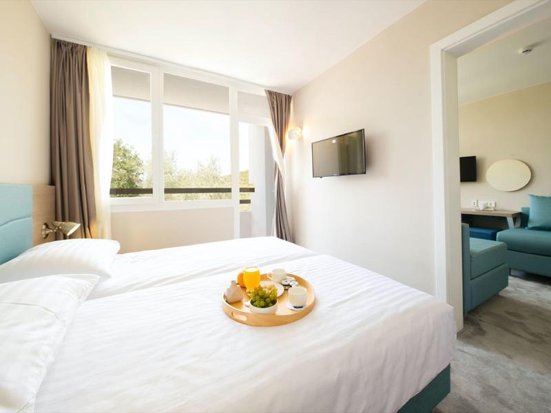 Helles Hotelzimmer mit Doppelbett und Frühstückstablett, Blick ins angrenzende Wohnzimmer.