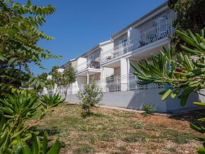 Modern wit appartementencomplex met balkons, omgeven door struiken en een helderblauwe lucht.