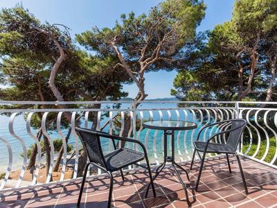 Balkon mit zwei schwarzen Stühlen, weißem Geländer, Pinien und Meer im Hintergrund bei Sonnenschein.