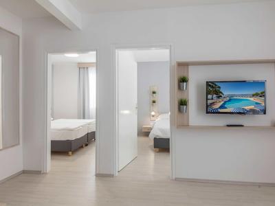 Chambre d'hôtel moderne avec deux chambres, murs clairs et grand téléviseur.