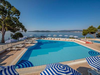 Piscine avec parasols bleus et blancs au bord de la mer sous un ciel clair.