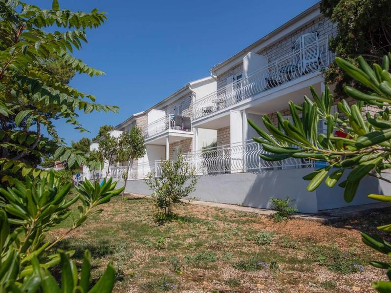 Modern wit appartementencomplex met balkons, omgeven door struiken en een helderblauwe lucht.