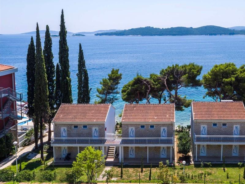 Drie rijtjeshuizen met uitzicht op de blauwe zee, omgeven door groene bomen en planten.