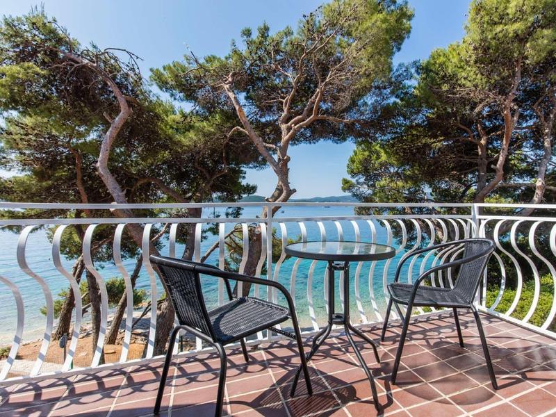 Balkon met twee stoelen en tafel met uitzicht op zee en pijnbomen.