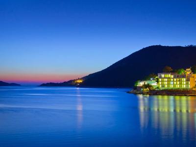 Hôtel côtier la nuit avec montagne et mer calme sous un ciel dégagé.