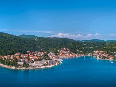 Coastal town with houses by the water, surrounded by wooded hills and blue sky.