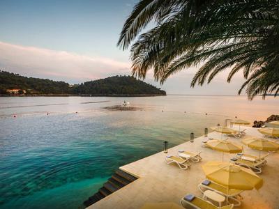 Blick auf ruhiges Meer mit Insel, Palmen und gelben Sonnenschirmen neben Liegestühlen am Ufer.