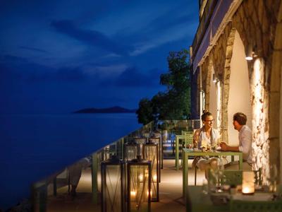 Couple enjoying a romantic dinner on a lit terrace by the water at sunset.