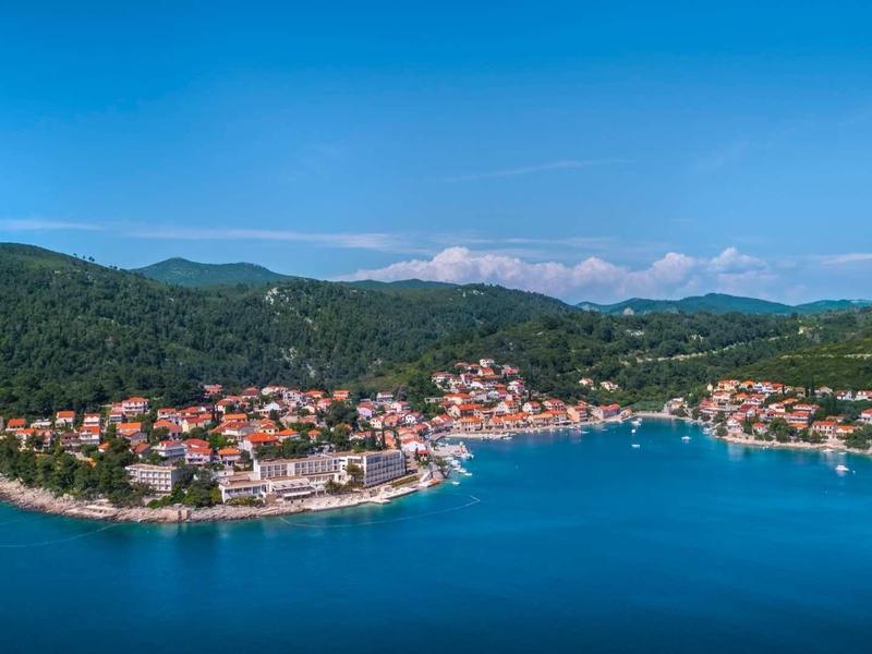 Coastal town with houses by the water, surrounded by wooded hills and blue sky.