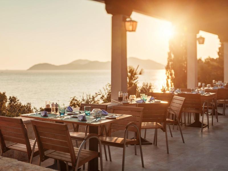 Terasa restaurace s dřevěnými židlemi s výhledem na moře při západu slunce.