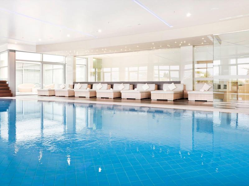 Světlý vnitřní bazén s modrými dlaždicemi a bílými sedacími oblastmi.