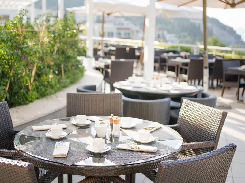 Venkovní stůl připravený s kávovými šálky a příbory na hotelové terase s výhledem na kopec.