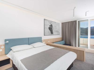 Moderní hotelový pokoj s manželskou postelí, velkým oknem a výhledem na moře.