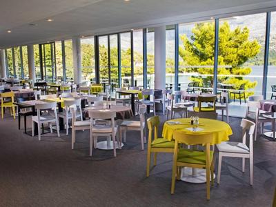 Světle osvětlená restaurace se žlutými a bílými stoly a velkými okny s výhledem na jezero.