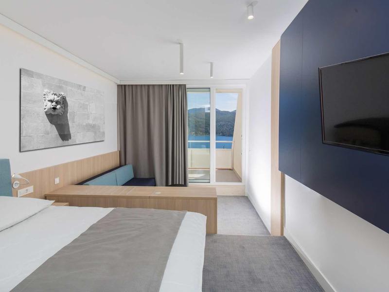 Modern hotel room with double bed, TV, and balcony overlooking the lake.