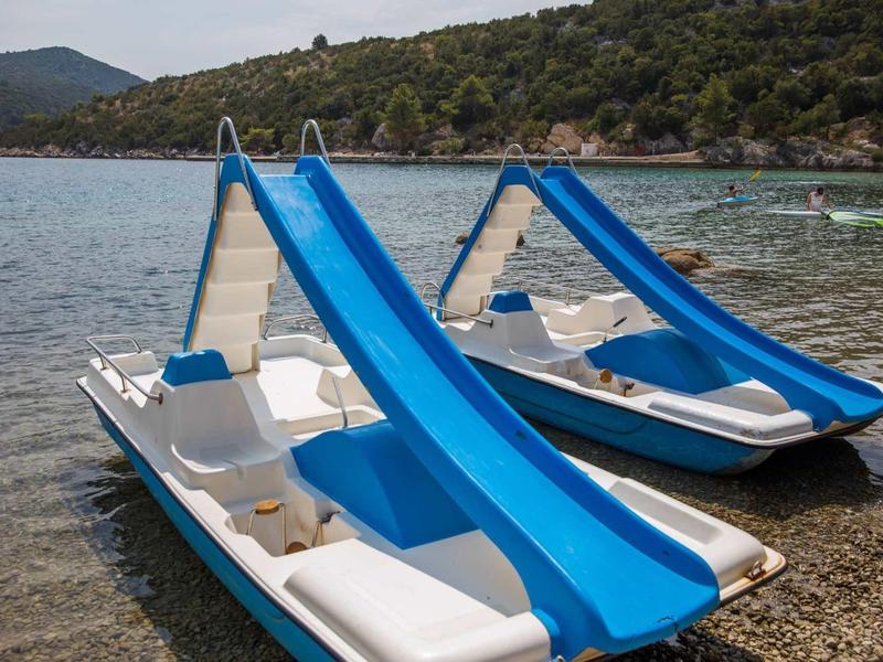 Two blue water slides on white pedal boats at the shore of a calm lake with wooded hills in the background.