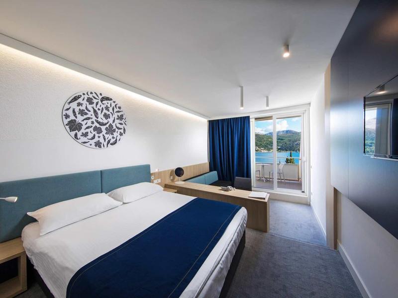 Modern hotel room with large bed, blue bedspread, and balcony access with a view.